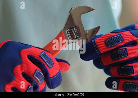 Primo piano delle mani del riparatore nei guanti che tengono la chiave. Foto Stock