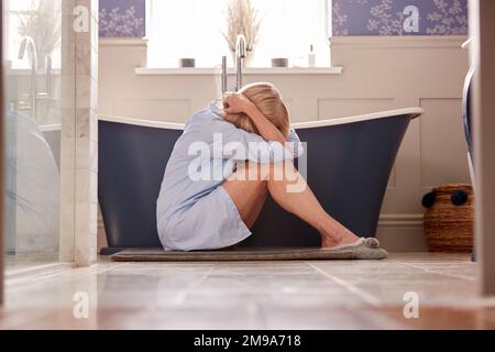 Menopausale Donna matura che soffre con incontinenza seduta sul pavimento del bagno a casa Foto Stock