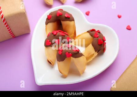 Piatto di gustosi biscotti di fortuna su sfondo lilla, primo piano. Festa di San Valentino Foto Stock