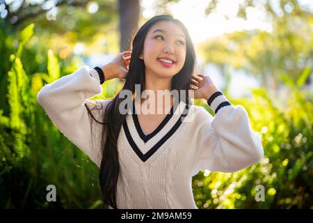 Ragazza adolescente che indossa un abito maglione in piedi di fronte a un giardino Fern con il sole di impostazione sullo sfondo Foto Stock