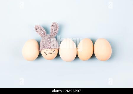 Cinque uova di Pasqua con volti divertenti e cappelli grigi con orecchie conigliate su sfondo blu. Buon concetto di Pasqua. Biglietto d'auguri. Foto Stock