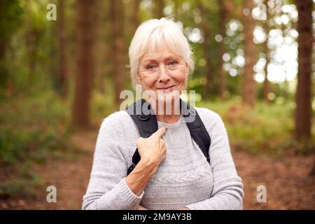 Ritratto di donna anziana in pensione attiva che cammina nella campagna di Woodland indossando lo zaino Foto Stock