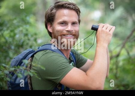 escursionista maschile guardando attraverso binocoli nella foresta Foto Stock