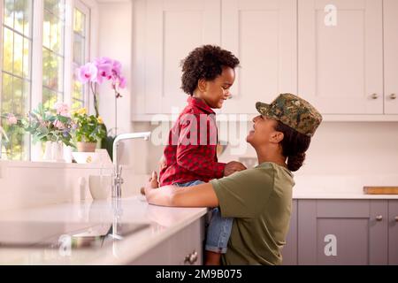 Amando la madre americana dell'esercito nella sede uniforme sul congedo con il figlio nella cucina della famiglia Foto Stock