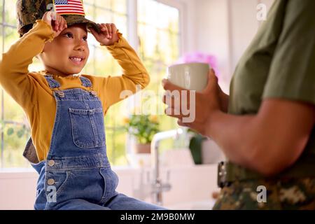 American Army Mother in uniforme Casa in congedo con la figlia che indossa il cappellino seduto in Family Kitchen Foto Stock