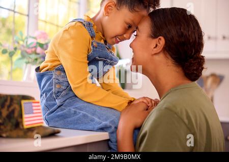 Amando la madre americana dell'esercito nella sede uniforme sul permesso che abbraccia la figlia in cucina della famiglia Foto Stock