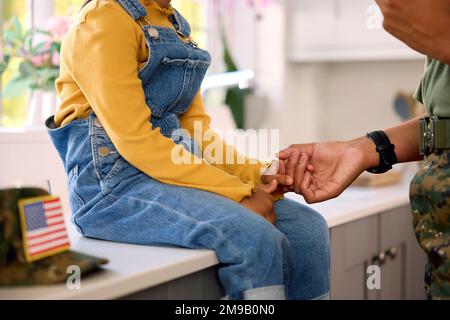 Amando la madre americana dell'esercito nella sede uniforme sul permesso che tiene le mani con la figlia in cucina della famiglia Foto Stock