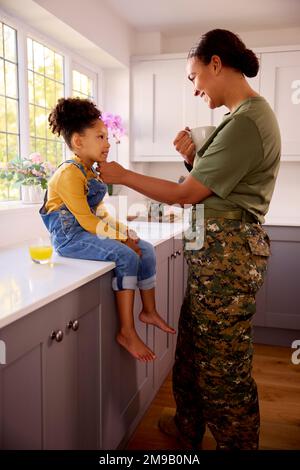 Amando la madre americana dell'esercito nella sede uniforme sul congedo con la figlia in cucina della famiglia Foto Stock