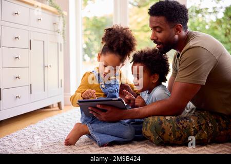 Army Padre in uniforme Casa in congedo con i bambini che utilizzano il tablet digitale Foto Stock