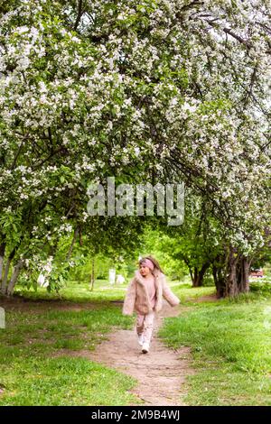 ragazza in una giacca soffice cammina in un parco con alberi in fiore in primavera Foto Stock