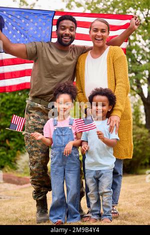 Ritratto di American Army Family Outdoors in Garden Holding Stars and Stripes Flag Foto Stock