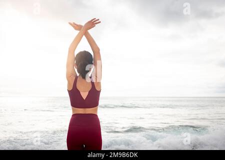 Donna che fa meditazione yoga guardando fuori al mare, vista posteriore. Foto Stock