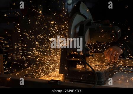 La sega taglia il metallo. Scintille dovute all'attrito. Lotto di scintille da segare l'acciaio. Funzionamento dell'attrezzo in garage. Foto Stock