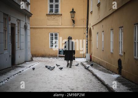 Un uomo cammina per una strada vuota a Praga. I piccioni mangiano il grano nella strada. Foto Stock