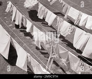 1950S 1960S VESTITI APPENA LAVATI LENZUOLA LAVANDERIA ASCIUGAMANI APPESI SU UNA LINEA DI VESTITI IN CORTILE CALDO LUMINOSO SOLE MITE BREASE - H2904 DEB001 HARS VECCHIO STILE Foto Stock