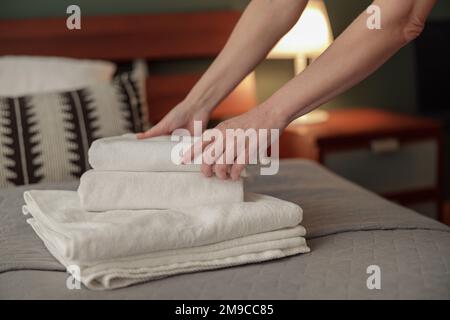 Primo piano delle mani della cameriera mettendo una pila di asciugamani bianchi freschi sulla biancheria da letto. Concetto di servizio in camera Foto Stock