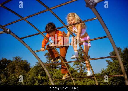 1970S RAGAZZO E RAGAZZA CHE GIOCANO ARRAMPICATA MONKEY BAR AL PARCO GIOCHI - KJ6857 KRU001 HARS CONCORSO FELICE GIOIA LIFESTYLE SODDISFAZIONE FEMMINE FRATELLI COPY SPAZIO AMICIZIA FULL-LENGTH PERSONE MASCHI FRATELLI SORELLE BAR ESTATE ALLEGRA AVVENTURA ED ECCITAZIONE LOW ANGLE RICREAZIONE FRATELLO SORRISI CONNESSIONE AMICHEVOLE STAGIONE GIOIOSA CAUCASICA ETNICITÀ GRIGLIA SCIMMIA BAR VECCHIO STILE Foto Stock