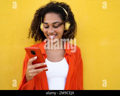 Allegra giovane donna chiacchiera con il telefono cellulare sopra il muro giallo in città Foto Stock