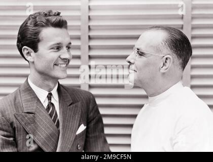 1930S 1940S GIOVANE UOMO SORRIDENTE IN TUTA DA POLSO CHE PARLA CON MEDICO DI MEZZA ETÀ CHE INDOSSA OCCHIALI - M316 HAR001 FAMIGLIE HARS GIOIA LIFESTYLE SODDISFAZIONE STUDIO SHOT HEALTHINESS STRISCIA COPIA SPAZIO AMICIZIA PERSONE ISPIRAZIONE MASCHI CURA FIDUCIA EYEGLASSES PADRI DI MEZZA ETÀ B&W UOMO DI MEZZA ETÀ TUTA SANITARIA E LEGAME DI OCCUPAZIONE FELICITÀ TESTA E SPALLE FORNITORE DI FORNITORI ALLEGRI PROFESSIONISTI PAPÀ GUARIGIONE MEDICI CURE SANITARIE PROFESSIONI SORRISI CONNESSIONE GUARITORE PSINSTRIPE MEDICO GIOIOSO PROFESSIONISTA ELEGANTE PROFESSIONISTI INSIEME VENEZIANO TENDE GIOVANE UOMO ADULTO Foto Stock