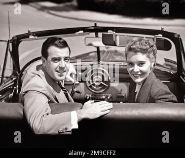 1950S UOMO E DONNA SORRIDENTI SEDUTI SUL SEDILE ANTERIORE DI UN'AUTO CONVERTIBILE SI VOLTÒ GUARDANDO LE SPALLE E LO SCHIENALE LA MACCHINA FOTOGRAFICA - M3495 HAR001 HARS LADIES PERSONE MASCHI B&W PARTNER ALLEGRO E SORRISI GIRATI GIOIOSO MOGLI GIOVANE ADULTO GIOVANE DONNA ADULTA NERA E BIANCA ETNIA CAUCASICA HAR001 VECCHIO STILE Foto Stock