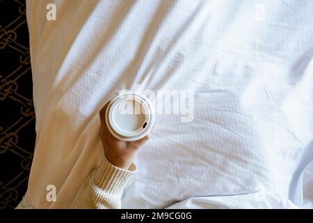 Donna che tiene la tazza di carta di caffè nel letto con il Lipstick Foto Stock