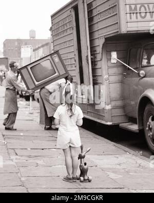 1970S BAMBINA CON IL SUO GIOCATTOLO DA TIRARE IN PIEDI SU CITY STREET GUARDANDO I MOTORI CARICARE UNA TELEVISIONE IN UN FURGONE IN MOVIMENTO - M9002 HAR001 HARS PULL LIFESTYLE FEMMINE LAVORI HOME VITA TRASPORTO COPIA SPAZIO TRASPORTO LUNGHEZZA INTERA CARICO B&W TRISTEZZA PROFESSIONE ABILITÀ ABILITÀ AVVENTURA CARICO VISTA POSTERIORE OCCUPAZIONI CONNESSIONE VISTA POSTERIORE CRESCITA GIOVANI MOVERS TRASFERIMENTO NERO E BIANCO ETNICITÀ CAUCASICA HAR001 ANNI MODELLATO Foto Stock