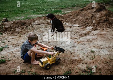 Ragazzo che gioca a trattori in terra nel cortile a casa Foto Stock