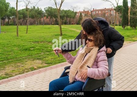 una ragazza che scatta foto con la nonna in sedia a rotelle Foto Stock