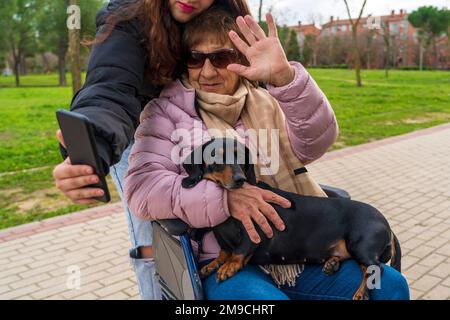 una ragazza che scatta foto con la nonna in sedia a rotelle Foto Stock