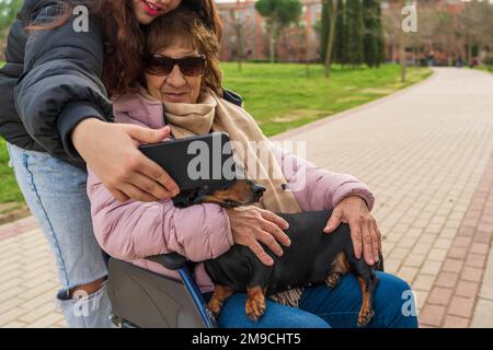 una ragazza che scatta foto con la nonna in sedia a rotelle Foto Stock