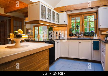 Cucina con isola in legno d'acero, armadi in legno bianco e ripiani in granito nero all'interno di una casa in legno di stile canadese. Foto Stock