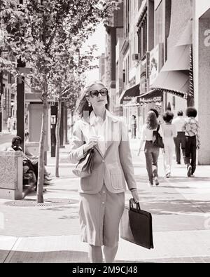 1970S DONNA D'AFFARI CHE INDOSSA OCCHIALI DA SOLE CHE TRASPORTANO LA VALIGETTA CHE CAMMINA GIÙ LA CITTÀ STREET - S20454 HAR001 HARS CARRIERA LIFESTYLE SODDISFAZIONE DONNE LAVORI COPY SPAZIO METÀ LUNGHEZZA SIGNORE PERSONE PROFESSIONE BLAZER FIDUCIA B&W BUSINESSWOMAN ABILITÀ PROFESSIONE PEDONE VENDERE ABILITÀ STILI AVVOCATI CARRIERE LEADERSHIP ORGOGLIO AVVOCATI OPPORTUNITÀ OCCUPAZIONI CITTÀ VENDITORE SALESWOMEN ELEGANTE DONNE D'AFFARI REVERS AVVOCATO MODA DONNA MEDIO-ADULTO DONNA NERO E BIANCO CAUCASICA ETNIA HAR001 STOREFRONTS VECCHIO STILE Foto Stock