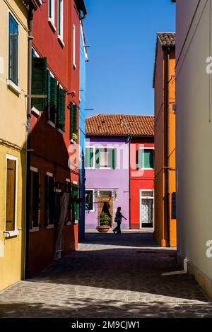 Una silhouette di una donna italiana locale mentre cammina tra i colorati edifici tradizionali del villaggio isolano di Burano, Italia. Foto Stock