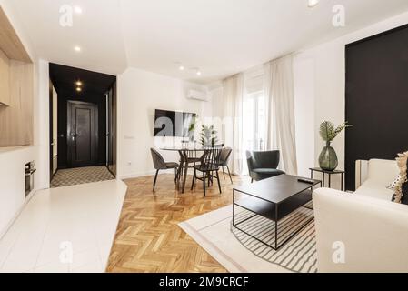 Loft con tavolo da pranzo nero rotondo in vetro con vaso e cucina a pianta aperta in design contemporaneo, tv a parete e balcone con lenzuola Foto Stock