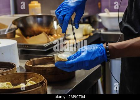 Uno chef asiatico con mani in guanti che prepara gnocchi per la consegna a domicilio Foto Stock