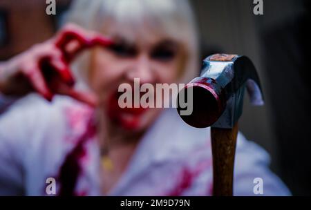 donna dai capelli bianchi che tiene un martello sanguinoso Foto Stock