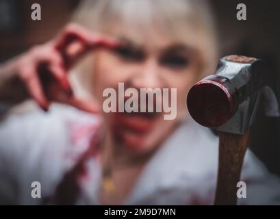 donna dai capelli bianchi che tiene un martello sanguinoso Foto Stock