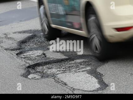 PRODUZIONE - 06 gennaio 2023, Hessen, Francoforte sul meno: Un'auto conduce nella città di Mörfelder Landstraße, nel quartiere Sachsenhausen, attraverso una pozza (ripresa con una velocità dell'otturatore maggiore). La strada ha numerose buche su una distanza di poco meno di un centinaio di metri. Il gelo delle ultime settimane ha colpito le strade. (A dpa 'buche e solchi: L'inverno rende necessarie riparazioni stradali') Foto: Arne Dedert/dpa Foto Stock