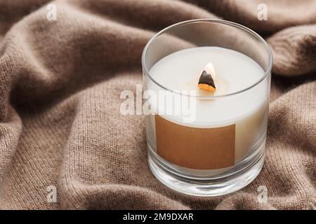 Una candela brucia sullo sfondo di un maglione lavorato a maglia. Il concetto di inverno o autunno accogliente. Foto Stock