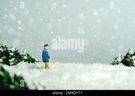 Fotografia di figura giocattolo delle persone in miniatura. Problema di mobilità durante l'inverno. Un vecchio che cammina in una nevicata sulla strada. Foto dell'immagine Foto Stock