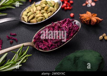 Varietà di spezie in cucchiai metallici paprika, curcuma, cardamomo, una miscela di spezie, timo, rosmarino e sale su fondo di cemento scuro Foto Stock