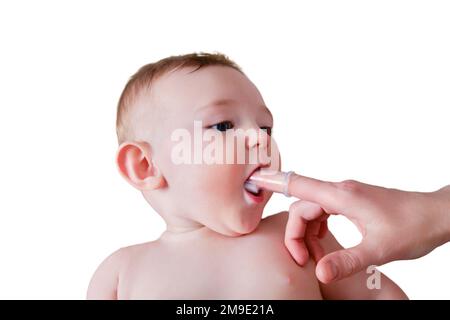 Le mani della madre spazzolano i denti con una spazzola per le dita di un bambino felice, isolato su uno sfondo bianco. Mamma che fa igiene orale a un bambino sorridente ki Foto Stock