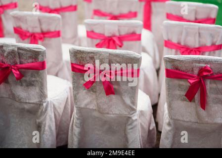 sedie per cerimonia nuziale decorate con tessuto bianco e nastri rosa Foto Stock