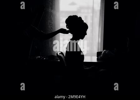 sposa fare i capelli per lo styling delle nozze con l'aiuto della vernice, la silhouette di fronte alla finestra Foto Stock