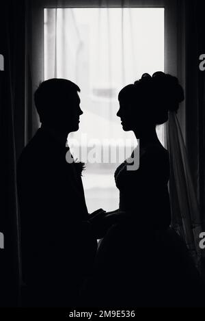 silhouette bianca e nera di una coppia in sposa d'amore e sposo il giorno del matrimonio di fronte alla finestra Foto Stock