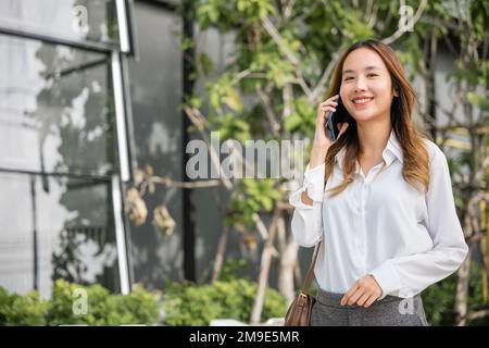 Bella giovane donna asiatica che chiama e parla al telefono o cellulare in città Foto Stock