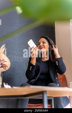 Donna di etnia latina in un deposito estetico di sopracciglia e unghie. In sala d'attesa parlando al telefono Foto Stock