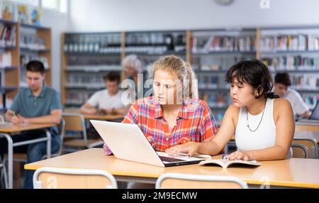 Ritratto di studentessa asiatica con un'amica spagnola che studia in biblioteca utilizzando il computer portatile Foto Stock