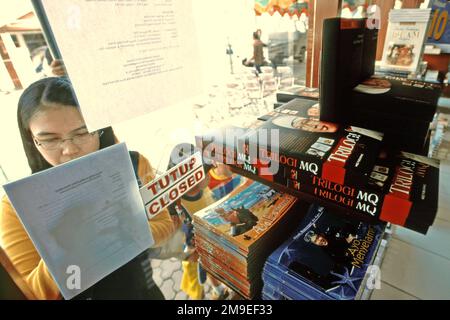 Una donna è fotografata da dietro il vetro di una libreria gestita da Manajemen Qolbu (mq), una filiale di gestione di Daaut Tauhiid, un'istituzione islamica fondata dal famoso predicatore islamico indonesiano, KH Abdullah Gymnastiar, situata a Gegerkalong, Bandung, West Java, Indonesia. Gymnastiar (popolarmente noto come AA Gym), Daarut Tauhiid, e il loro ramo di gestione Manajemen Qolbu (mq), sono riusciti a intensificare il turismo religioso e le attività economiche nella zona di Gegerkalong a Bandung City. Foto Stock