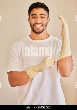Il suo giorno di lavoro. un bel giovane uomo che si alza da solo e indossa i guanti prima di pulire la sua casa. Foto Stock